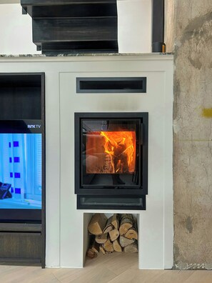 A modern fireplace with a TV screen displaying a blue screen, logs stored below, and a white wall. - Architect-designed flat on St. Hanshaugen (Oslo)