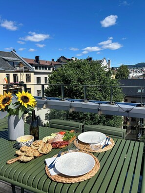 A rooftop terrace with a table set for two, featuring a variety of food items and a bottle of wine. - Architect-designed flat on St. Hanshaugen (Oslo)