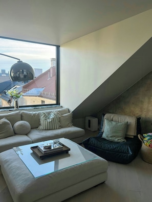 A modern loft bedroom with a sloped ceiling, a large window, a sofa, a coffee table, and a black leather chair. - Architect-designed flat on St. Hanshaugen (Oslo)