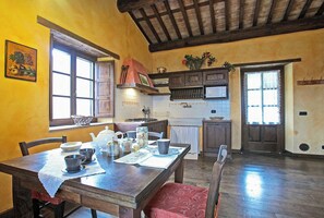 A dining area with a wooden table set for two, a kitchen with wooden cabinets, and a window with a view. - Tuscan casale with hot tub, pool and valley views (Sillico)