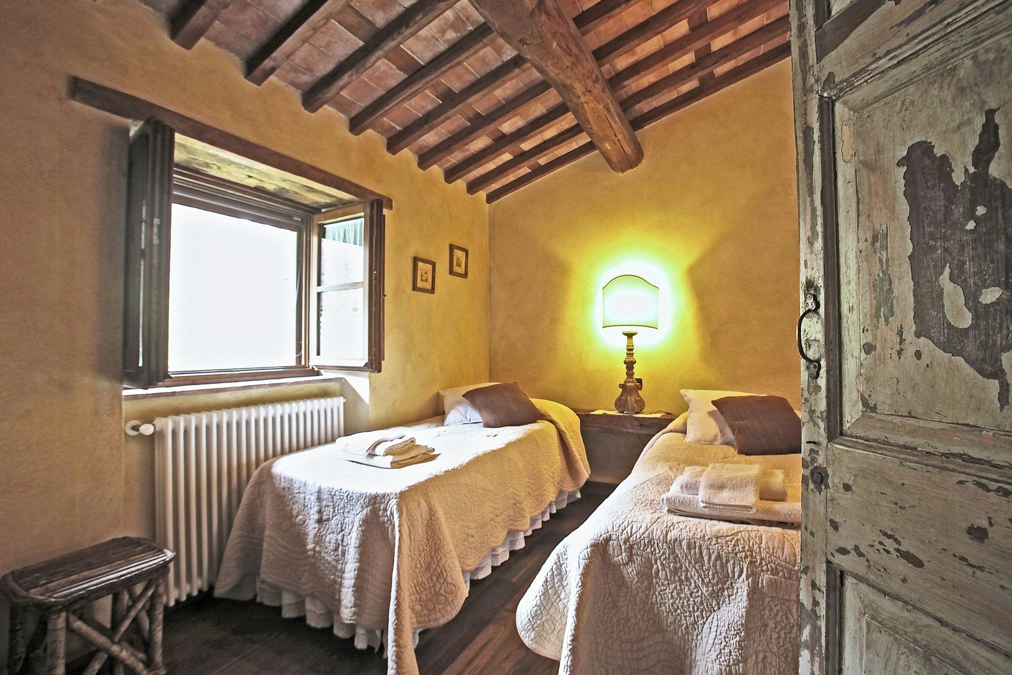 Une chambre avec deux lits, une fenêtre, un radiateur et une lampe.