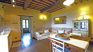A cozy living room with a sofa, wooden floor, and a dining area with a table and chairs. - Apartment in Tuscan farmhouse with pool and views (Sillico)