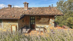 A stone house with a tiled roof, a chimney, and a small porch with outdoor seating. - Apartment in Tuscan farmhouse with pool and views (Sillico)