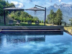 A pool with a wooden deck, two umbrellas, and chairs. - Apartment with Jacuzzi and pool on Tuscan hilltop (Sillico)