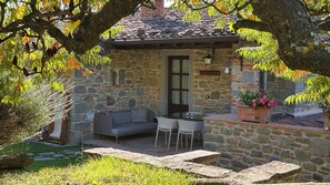 Un bâtiment en pierre avec un toit recouvert de tuiles, une table en verre et un canapé gris.