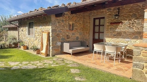 A stone building with a patio area, a sofa, and a table with chairs. - Apartment with Jacuzzi and pool on Tuscan hilltop (Sillico)