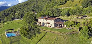 Une maison en pierre avec une piscine, entourée d’une végétation luxuriante et de collines.