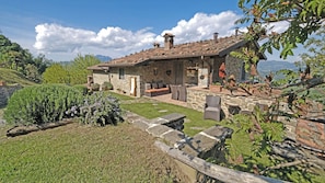 A stone house with a tiled roof, a stone patio, and a view of the mountains. - Apartment with Jacuzzi and pool on Tuscan hilltop (Sillico)