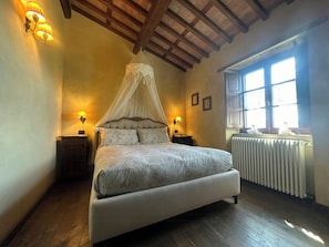 Une chambre à coucher avec un lit à baldaquin, deux lampes de chevet, une fenêtre donnant sur un beau paysage et un radiateur.