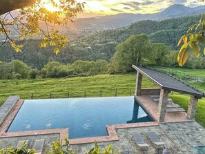 A swimming pool with a stone deck and lounge chairs, surrounded by a fenced area with a view of a mountainous landscape. - Apartment with Jacuzzi and pool on Tuscan hilltop (Sillico)