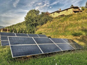 Solar panels on a grassy hillside with a stone building in the background. - Apartment with Jacuzzi and pool on Tuscan hilltop (Sillico)