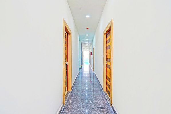 A corridor with wooden doors, white walls, and a marble floor.