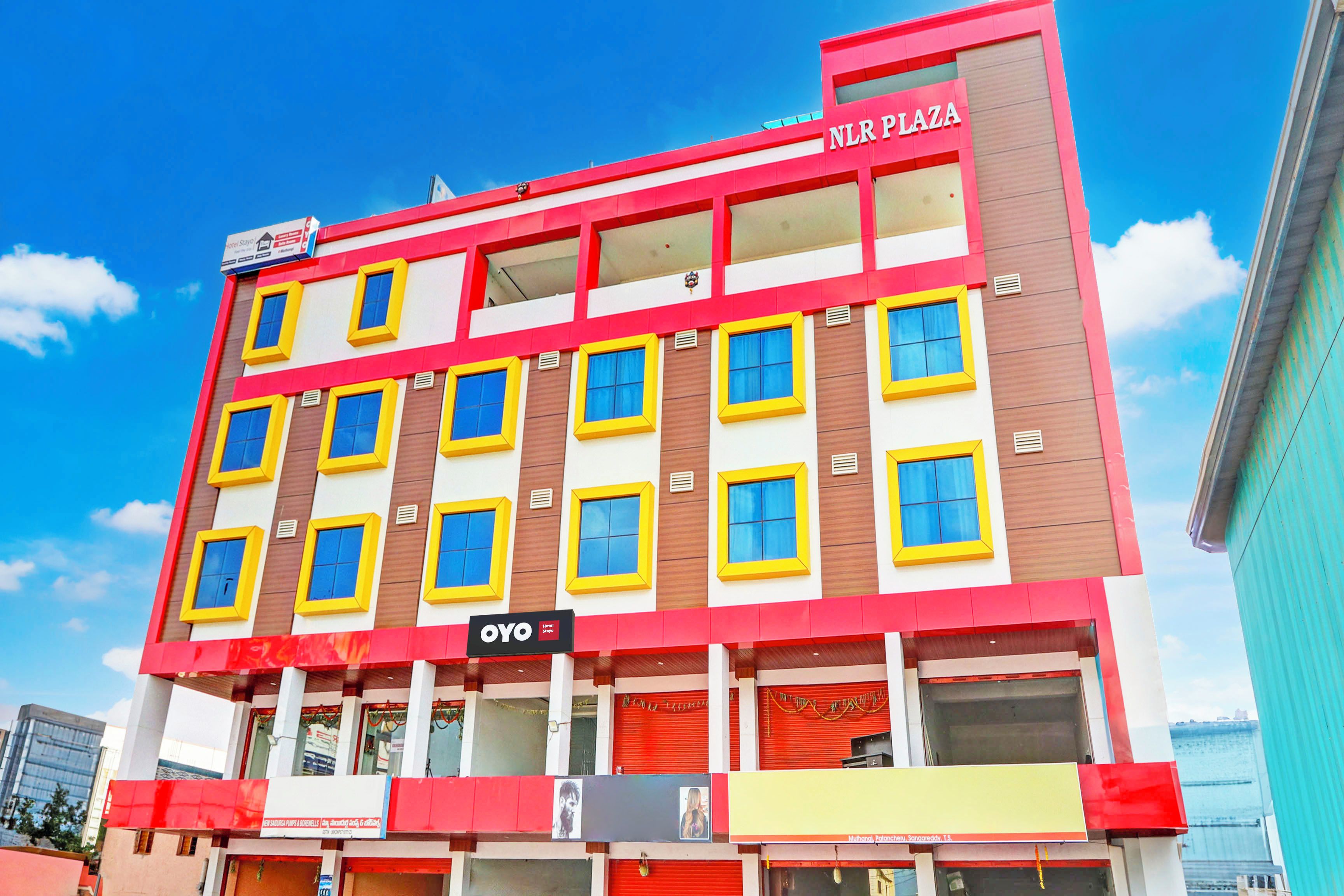 Un hotel de varios pisos con fachada roja y amarilla, múltiples ventanales y un letrero que dice 'NLR PLAZA'.