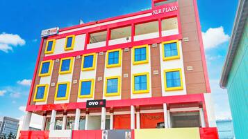 Un hotel de varios pisos con fachada roja y amarilla, múltiples ventanales y un letrero que dice 'NLR PLAZA'.