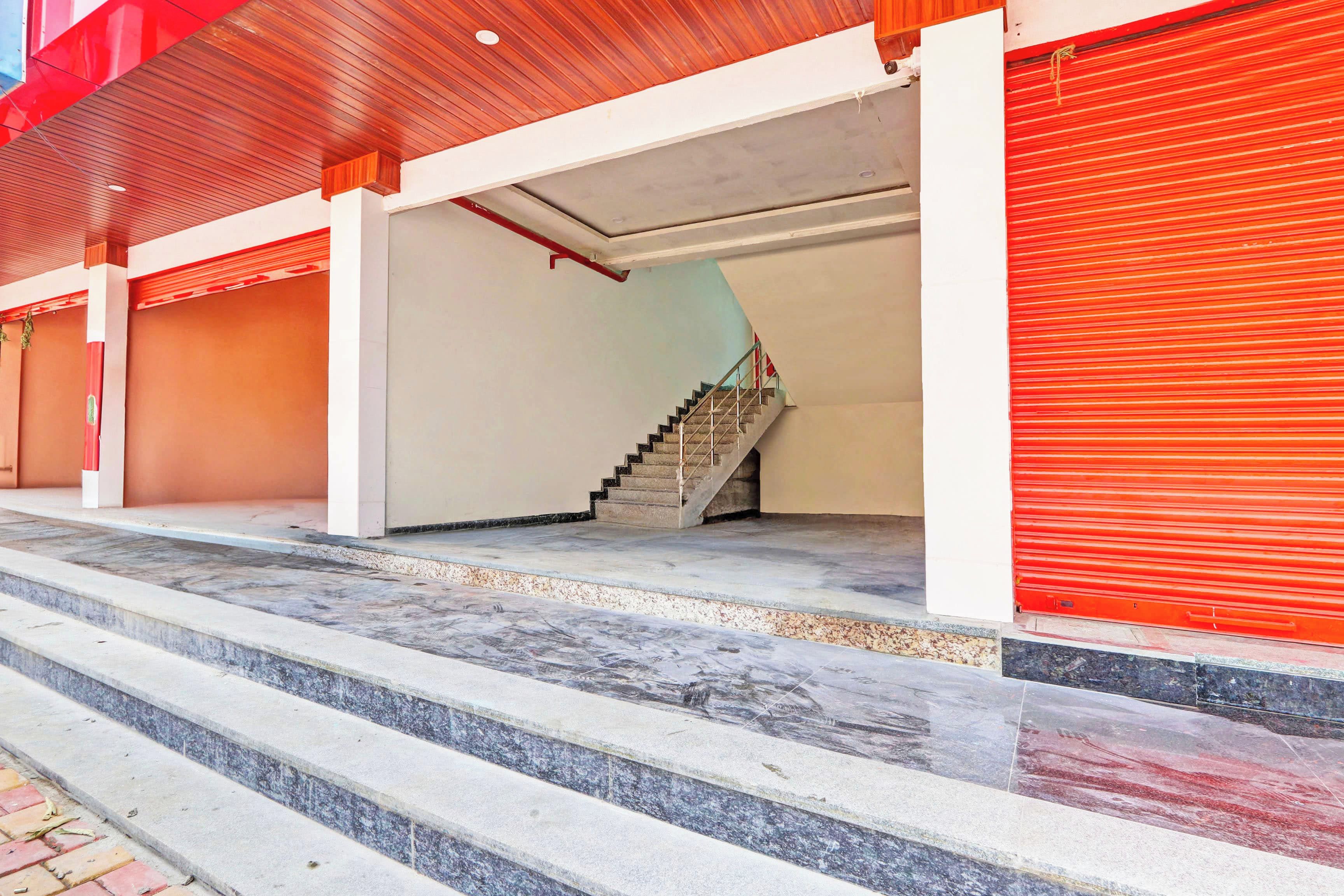 Um edifício com escadaria que dá para um patamar, entrada com persianas vermelhas e piso de concreto.
