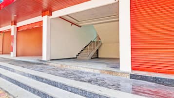 Um edifício com escadaria que dá para um patamar, entrada com persianas vermelhas e piso de concreto.