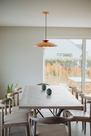 Un espace repas comprenant une longue table, des chaises et un luminaire suspendu.