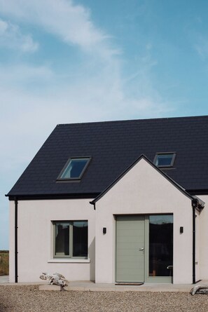 Une maison moderne à deux étages, dotée d’un toit en pente, de deux fenêtres à l’étage supérieur et d’une porte verte.