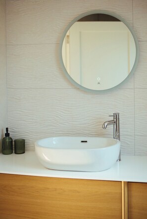 Une salle de bain avec un miroir rond, un lavabo blanc et un robinet chromé.