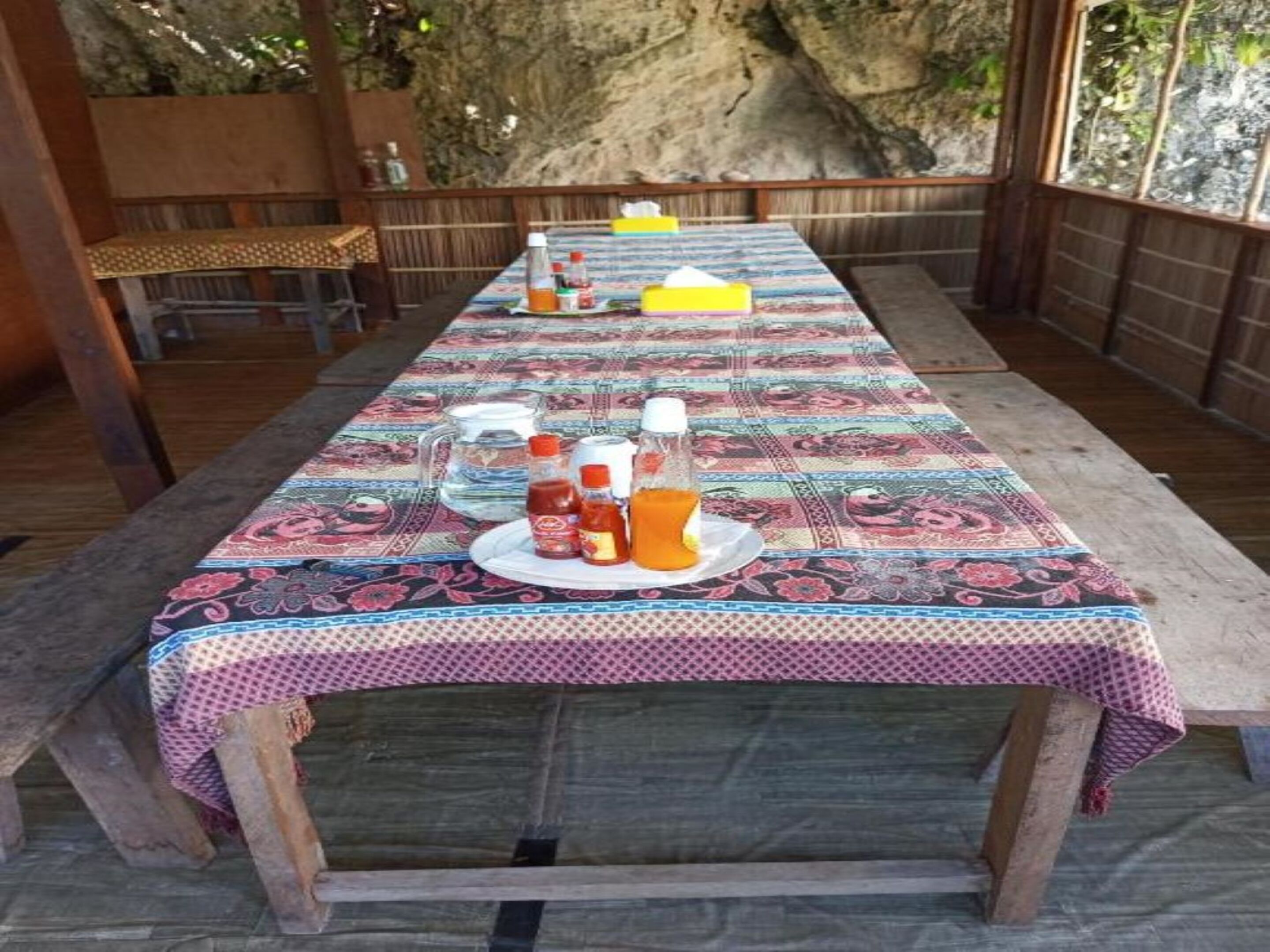 Een lange eettafel met een tafelkleed met patroon, omringd door houten stoelen.