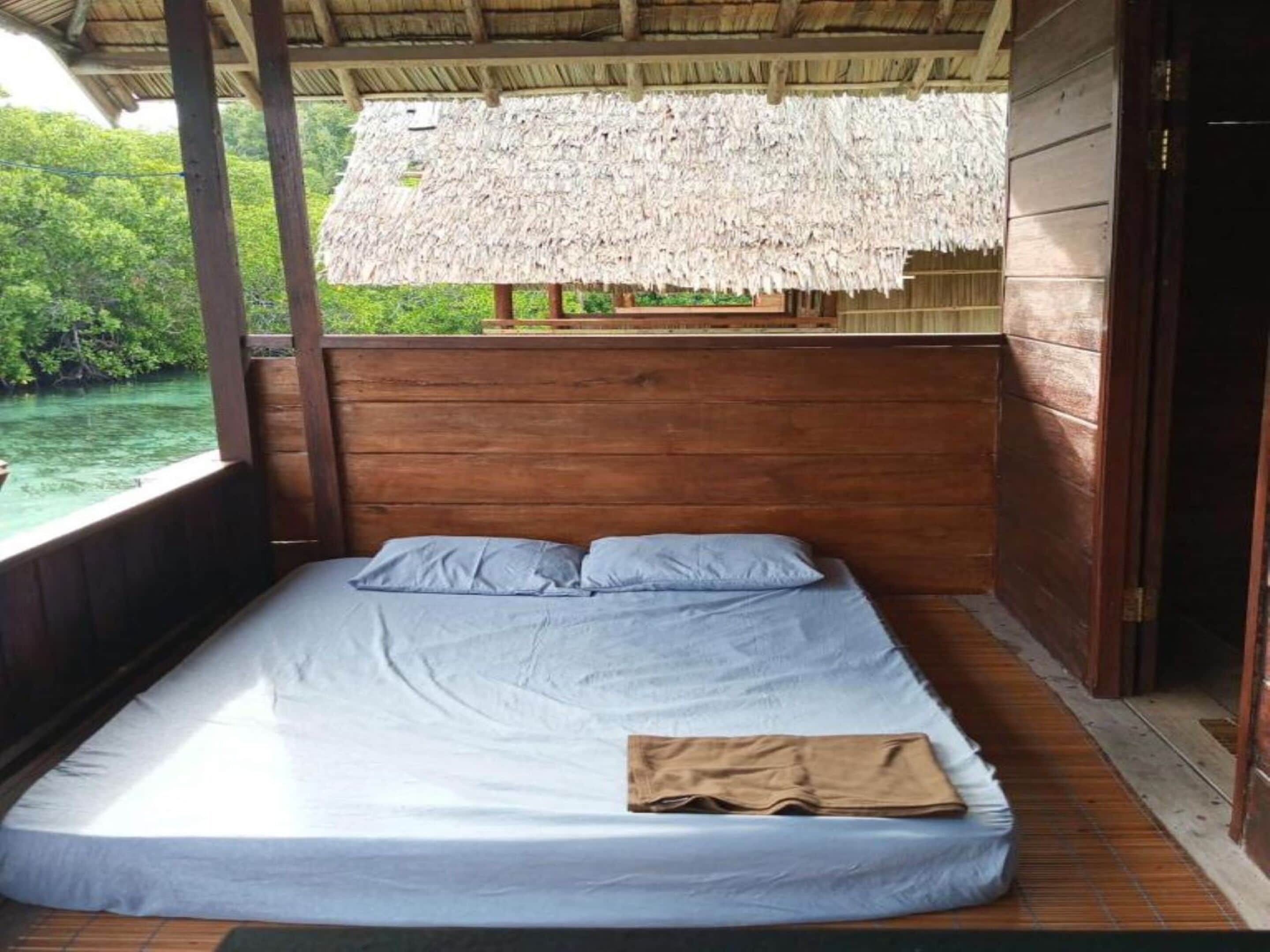 Un letto singolo con materasso e cuscini, pareti in legno e una struttura con tetto di paglia.
