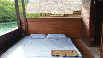 Un letto singolo con materasso e cuscini, pareti in legno e una struttura con tetto di paglia.