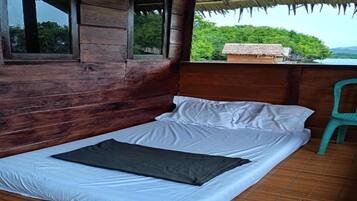 Una cama individual con ropa blanca y una manta oscura en una habitación de madera con vistas a zonas verdes.
