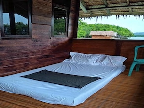 A single bed with white bedding and a dark blanket in a wooden room with a view of greenery. - Cozzy Anno Homestay (Sawinggrai)