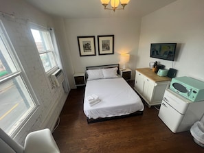 A hotel room with a bed, bedside table, lamp, microwave, and a view through a window. - Chic 420-Friendly LA Studio! Near Downtown! (Los Angeles)