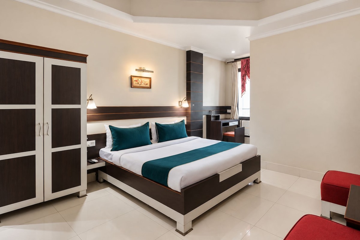 A modern hotel room with a large bed, a wardrobe, a desk, and a red chair.