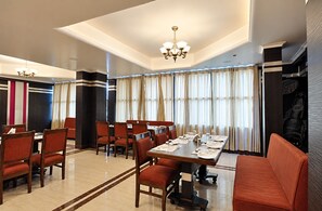 A dining area with a long table set for a meal, surrounded by chairs, and a chandelier above. - Hotel Star Regency (Prayagraj)
