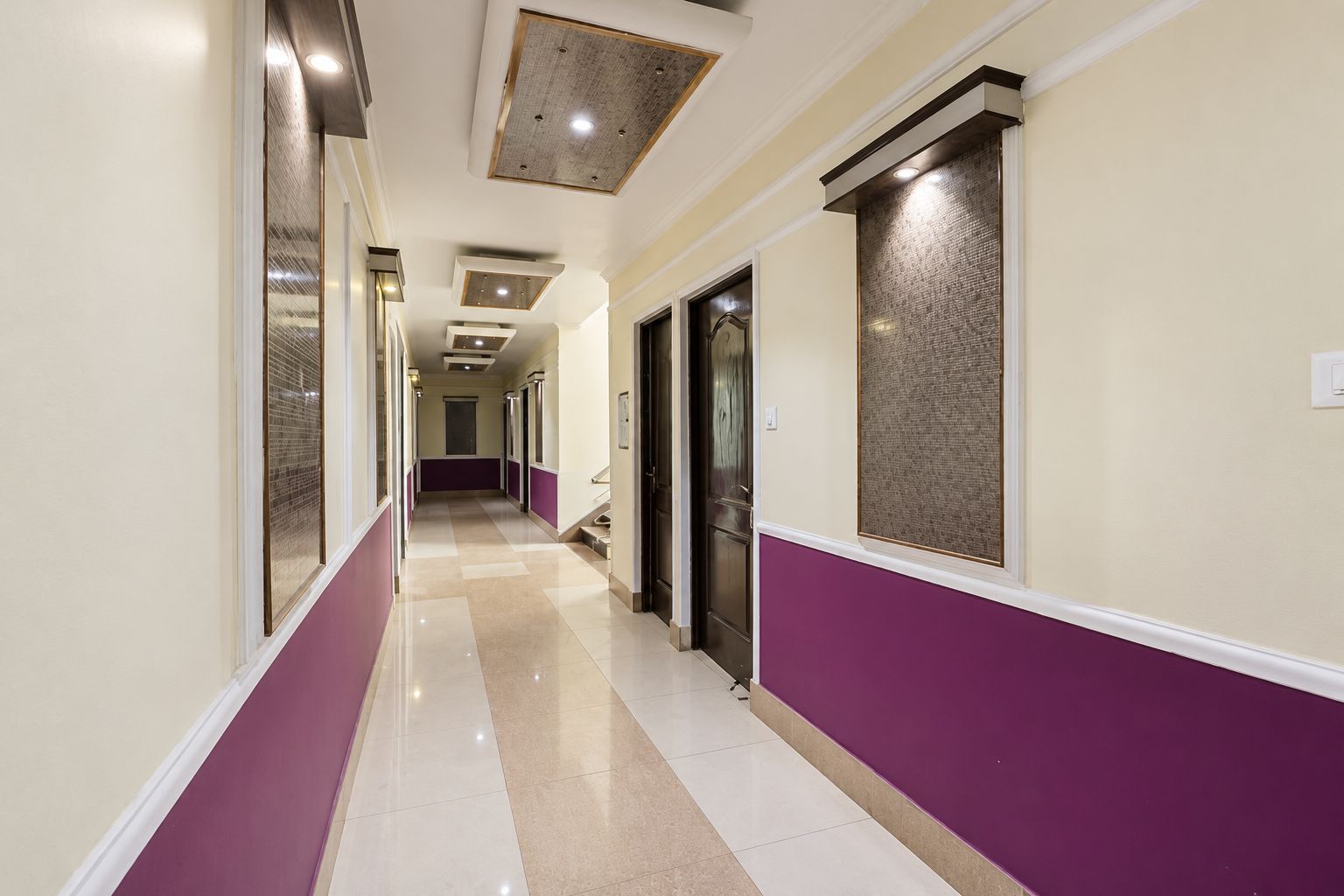 A hotel corridor with a checkered floor pattern, doors on both sides, and a ceiling with recessed lighting.