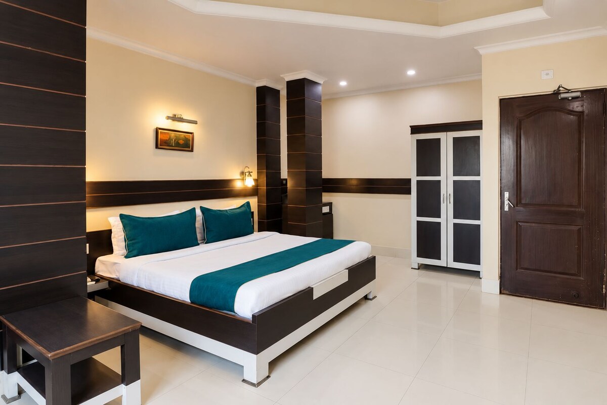 A modern hotel room with a large bed, a nightstand, a wardrobe, and a wall-mounted light fixture.