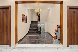A hotel lobby with a marble staircase, wooden doors numbered 103 and 104, a chandelier, and a decorative wall piece. - Collection O Sector 10 Greater Noida (Noida)