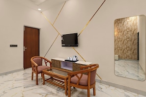 A hotel room with a wooden desk, two chairs, a flat-screen TV mounted on the wall, and a large mirror. - Collection O Sector 10 Greater Noida (Noida)