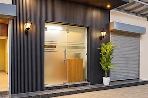 A modern building facade with a large glass door, two wall-mounted lights, and a potted plant. - Collection O Sector 10 Greater Noida (Noida)