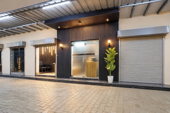 A modern building with a flat roof, a large entrance with a glass door, and a potted plant outside. - Collection O Sector 10 Greater Noida (Noida)