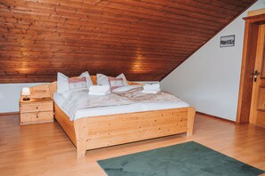 A wooden bed with a sloped ceiling, a nightstand, and a green rug. - 100 m² family apartment with south-facing balcony for up to 8 guests (Sankt Michael im Lungau)