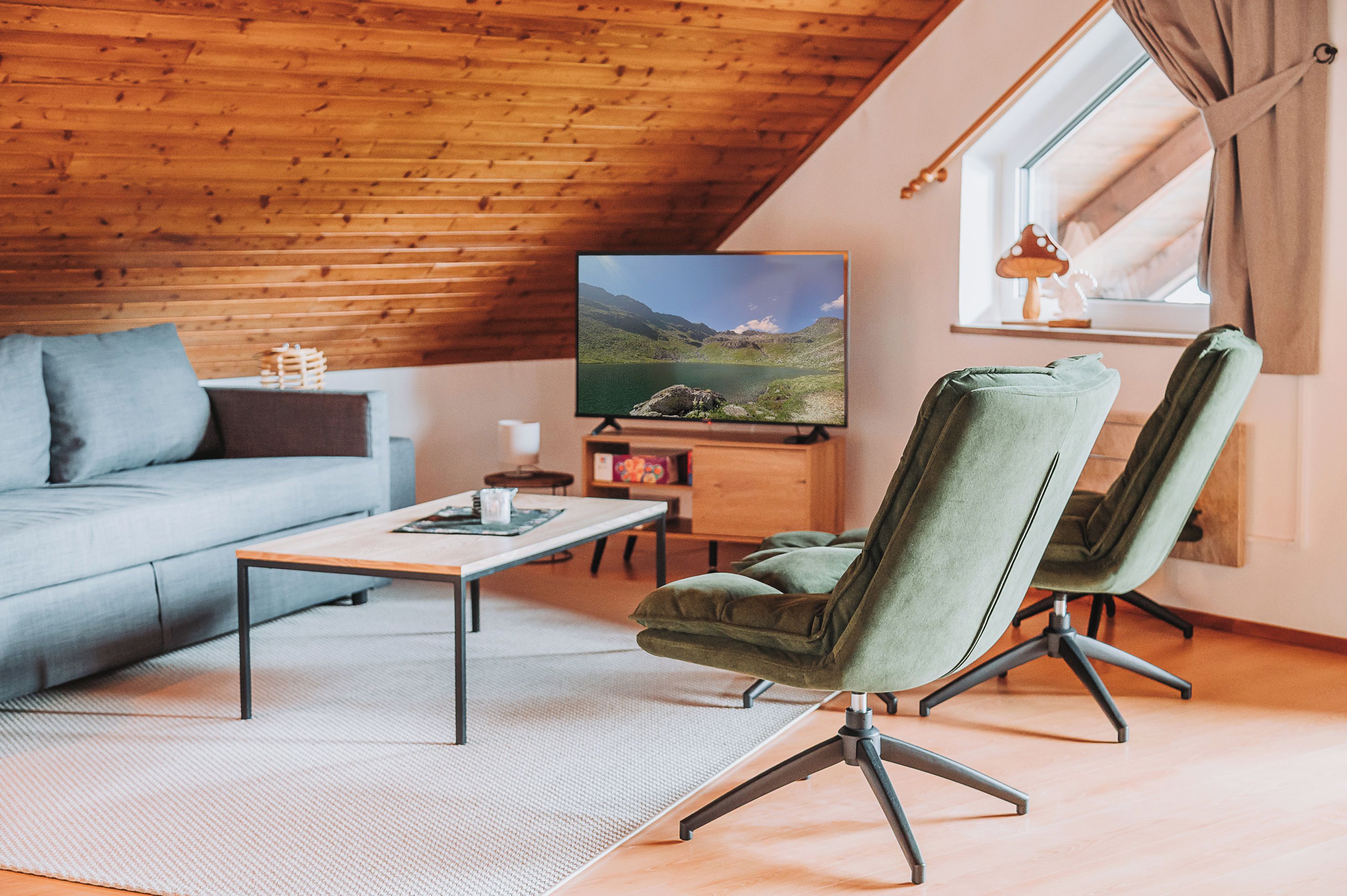 A cozy living room with a wooden ceiling, a sofa, a coffee table, and two green chairs.