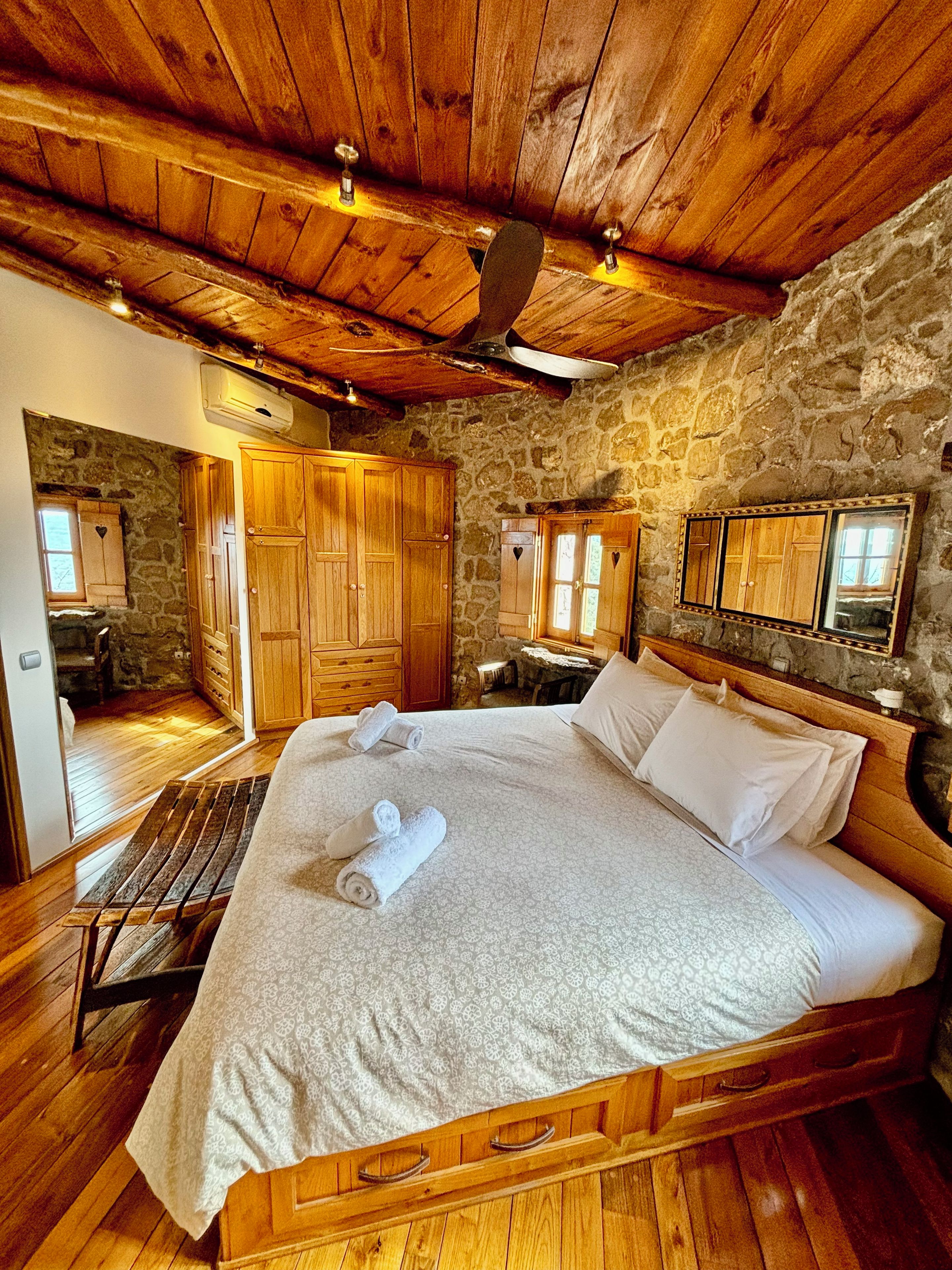 Une chambre avec un lit en bois, des murs en pierre et un plafond en bois.