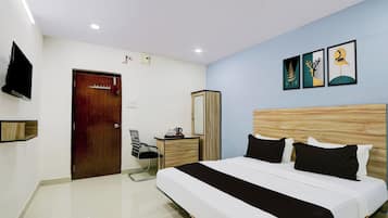 A modern hotel room with a large bed, a wooden headboard, a flat-screen TV mounted on the wall, and a small desk with a chair.
