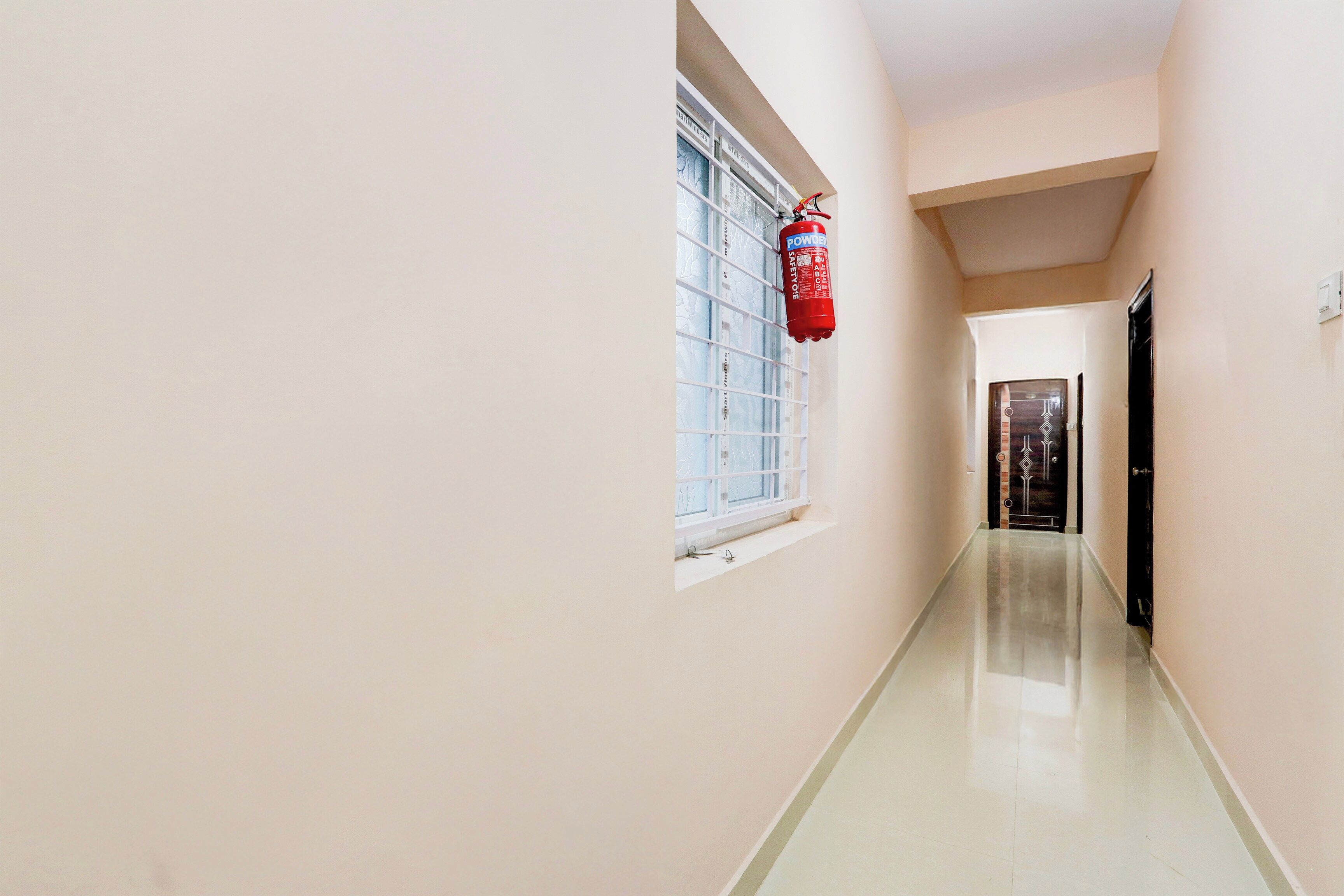 Un pasillo con un extintor montado en la pared, una ventana de celosía y una puerta al final.