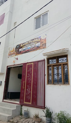 A building with a sign for 'Kashi Prabha Home Stay' and a red door with decorative patterns. - Kashi Prabha Homestay (Varanasi)