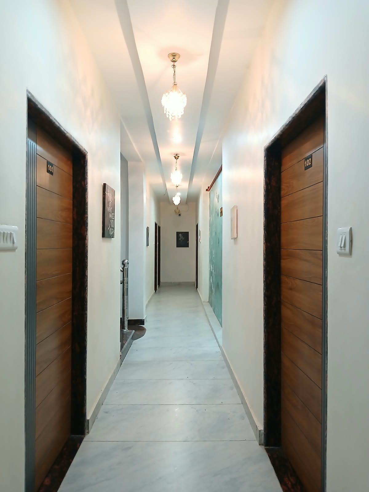 A hotel hallway with wooden doors numbered 101 and 102, a chandelier, and a tiled floor.