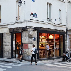 A street view of a building with a storefront that appears to be a restaurant or cafe, with outdoor seating visible. - Centrally Located 115SQM Residence In the Heart of Marais (Paris)