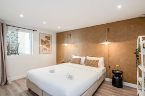 A modern bedroom with a large bed, two bedside lamps, a window with curtains, and a wall-mounted shelf with a plant. - Centrally Located 115SQM Residence In the Heart of Marais (Paris)