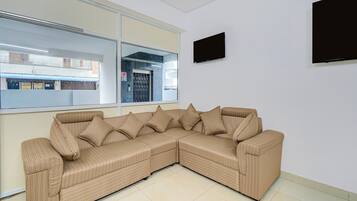 Un sofá de esquina con varios cojines en una habitación con un ventanal grande y un televisor de pantalla plana montado en la pared.