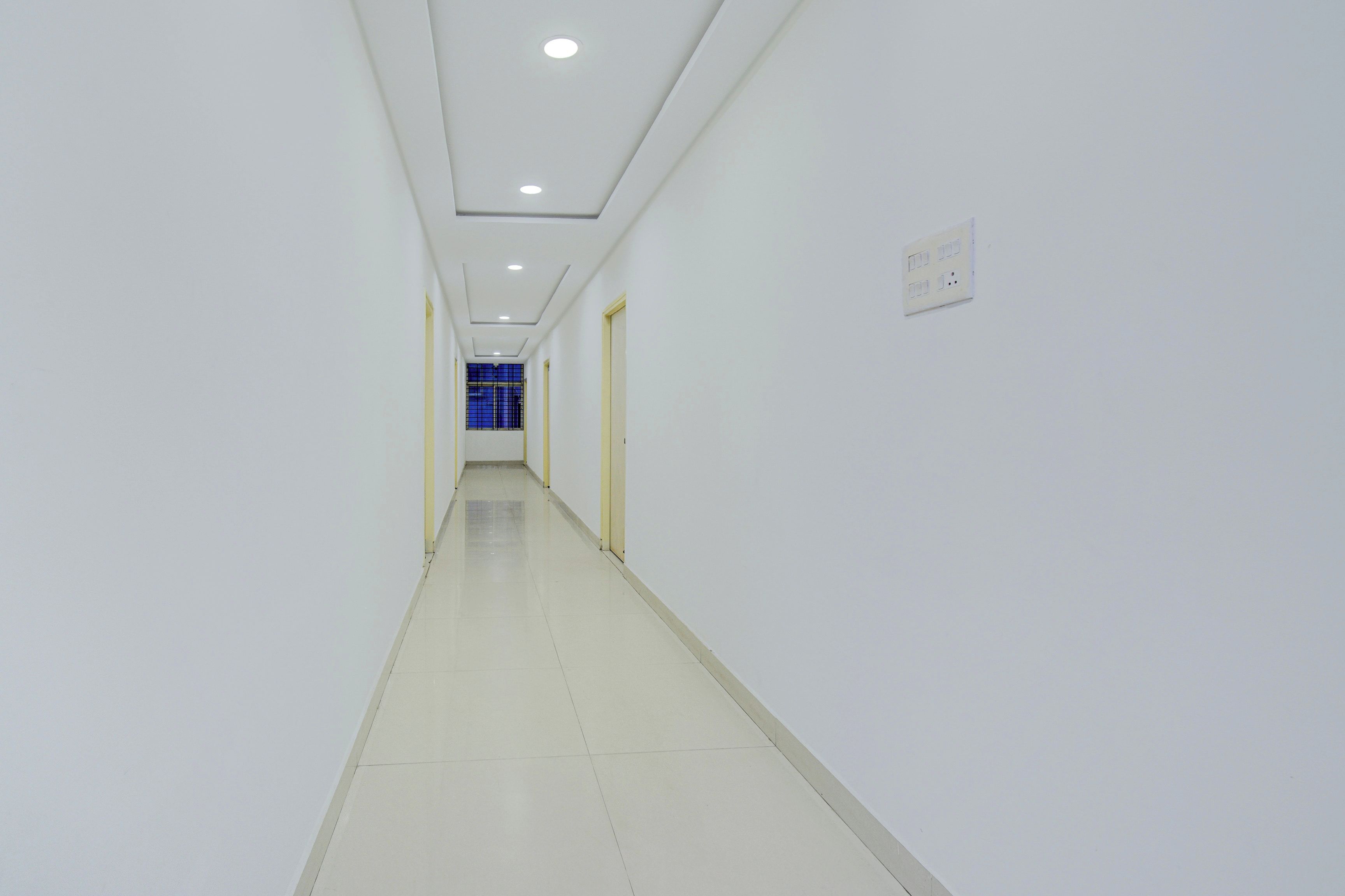 A long, narrow hallway with white walls and a tiled floor, leading to a door with a blue window.