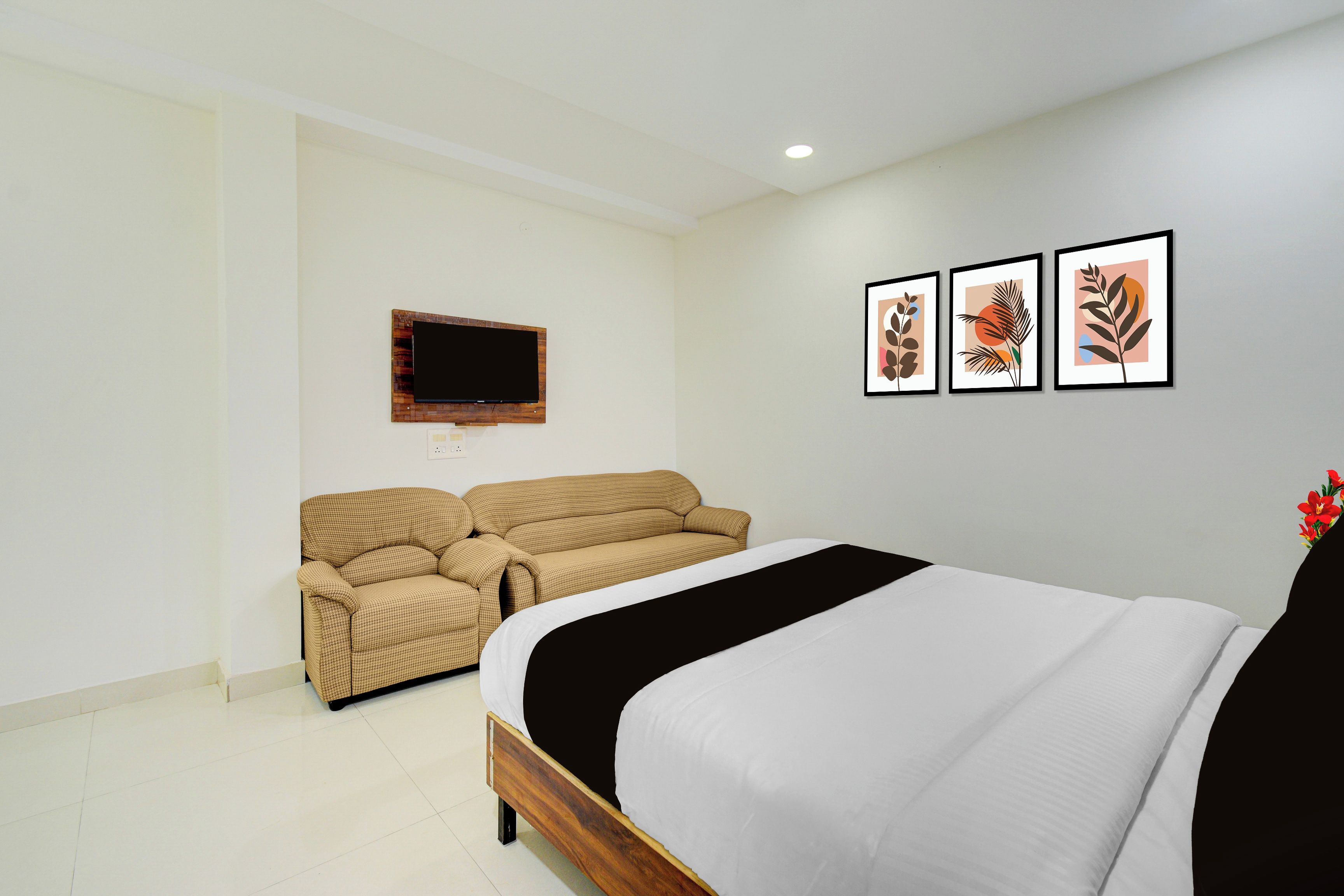 A bedroom with a bed, a sofa, a television, and three framed artworks on the wall.