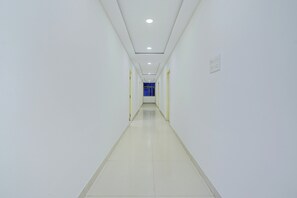 Un pasillo largo y estrecho con paredes blancas y piso de baldosas, que conduce a una habitación con un ventanal azul.